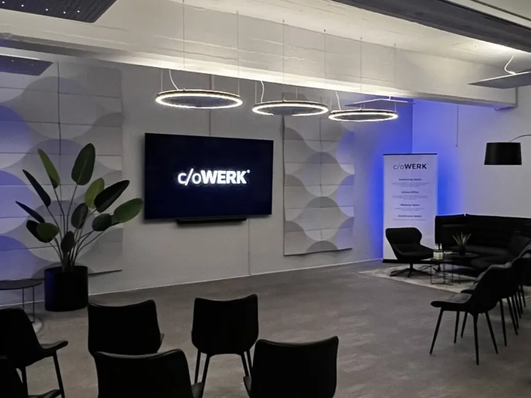 Konferenzraum im c/oWERK mit Stuhlreihen, zwei Bildschirmen und einer Sitzecke